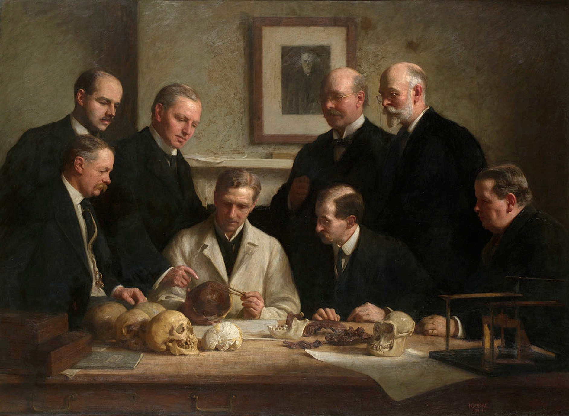 The Piltdown Gang, 1915 oil painting by John Cooke showing scientists examining the Piltdown skull fragments. Public domain.